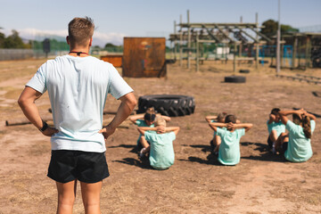 Rear view of male fitness coach and kids performing sit ups at a bootcamp