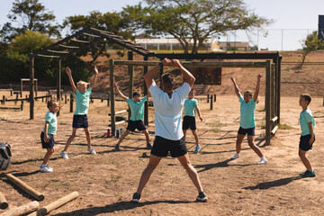 Male fitness coach and kids performing jumping jacks at a bootcamp