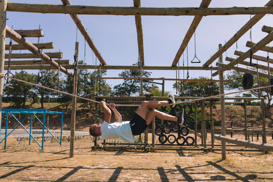 Male fitness coach hanging upside down on a rope at a boot camp