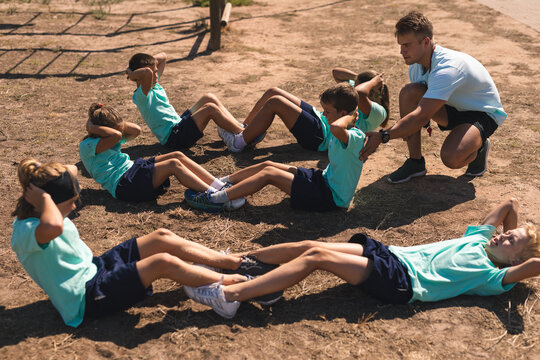 Male fitness coach instructing while kids performing sit ups at a boot camp - Powered by Adobe