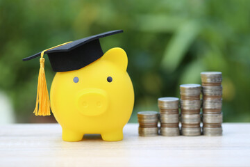 Graduation hat on golden piggy bank with stack of coins money on natural green background, Saving money for education concept