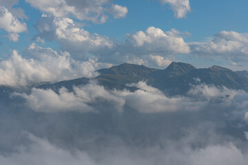 Fototapeta premium Rocky mountain peak, which rises in the middle of the prairie, in the Alps, between the grass on the slopes of the neighboring mountains and the cloudy sky with small blue glades. Gray rock peak.