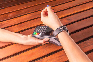 Payment for purchases using smart watches and POS terminal on wooden background. Contactless...