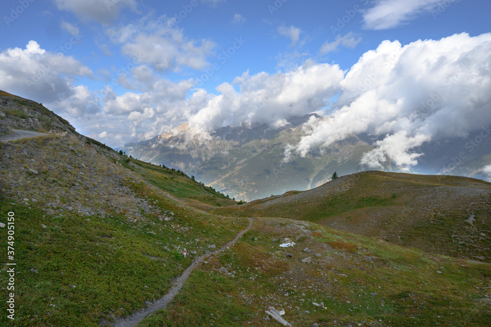 Wall mural footpath between the mountain peaks of the Alps, between the grass, ascending path to the cloudy mountains