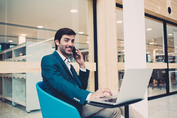 Portrait of successful South Asian employee in formal wear smiling at camera during business smartphone conversation, confident corporate boss have cellphone consultancy call during laptop work