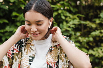 Optimistic young asian woman outdoors listening earphones