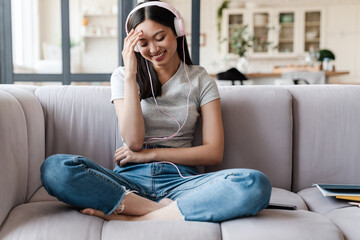 Fototapeta premium Image of woman listening music with headphones while sitting on sofa