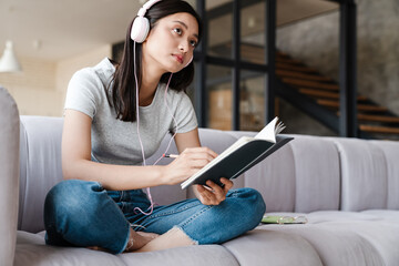 Obraz premium Image of focused asian woman using headphones and writing down notes
