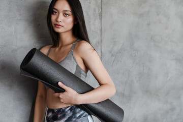 Image of beautiful asian girl in sportswear posing with yoga mat