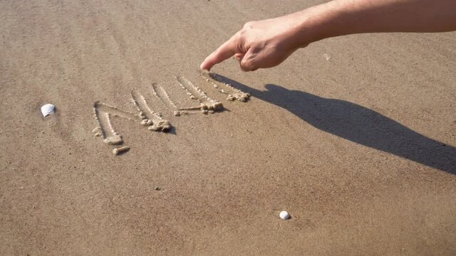Closeup of hand writing nude beach letters on sand at the beach on a sunny day. Naked sunbathing. Naturalist lifestyle.
