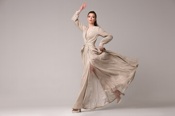 A girl in a long dress posing in the studio in full growth. She runs with her hand up, the ebka of...