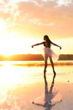 Silhouette of a slender girl ballerina dancing in a transparent airy dress against the backdrop of the setting sun.