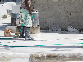 Black man construction worker produces the grout and finish wet concrete in outside with a special tool for smoothing and polishing concrete floors..