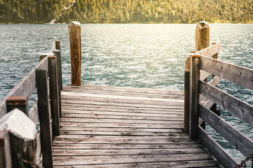 Fototapeta premium A wooden walkway with railings on a mountain lake in warm sunshine with a view of the mountains and the lake.