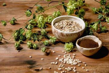 All for brewing. Fresh green hop cones, wheat grain and red fermented malt in ceramic bowls over wooden background.
