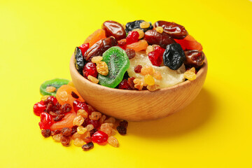 Wooden bowl with dried fruits on yellow background