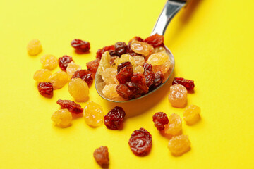 Spoon with raisins on yellow background, close up