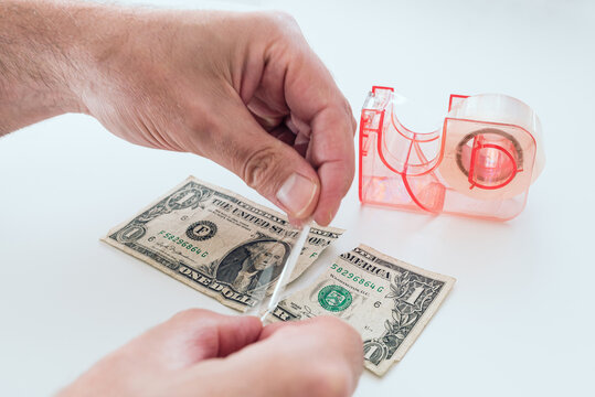 close-up of hands of man fixing old torn dollar bill with sticky tape on white desk