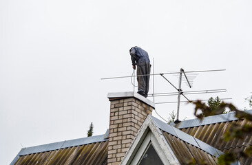 Chimney sweeper clears ash and soot from chimneys on cloudy autumn day.
