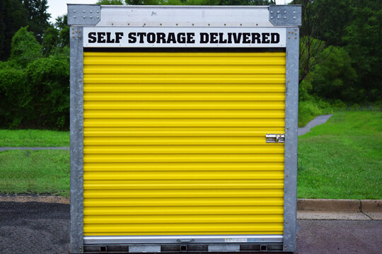 Portable Self-storage Unit On A Street Or Parking Lot.  Yellow Door And Locking Mechanism Visible. Metal Storage Shed Delivered To A Location.