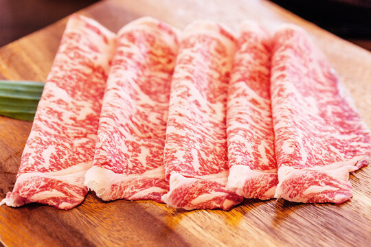 Crop image of Premium Rare Slices Wagyu A5 beef with high-marbled texture on square wooden plate served for Sukiyaki and Shabu.