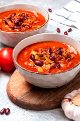 Chili con carne in a bowl on a grey concrete background close-up. Tex-mex food. Delicious spicy soup with red beans, peppers, tomatoes and minced meat.