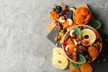 Board and bowls with dried fruits and nuts on gray background