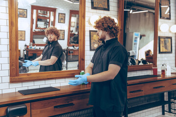 Male caucasian barber at the barbershop wearing gloves preparing working place for client. Professional barber wearing gloves. Covid-19, beauty, selfcare, style, healthcare and medicine concept.