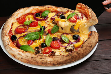 Woman taking slice of tasty vegetable pizza at wooden table, closeup