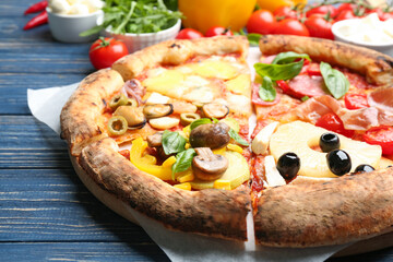 Slices of different pizzas on blue wooden table, closeup