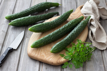 Long Chinese cucumbers laid out on a cutting board for slicing salad on the wooden background,...