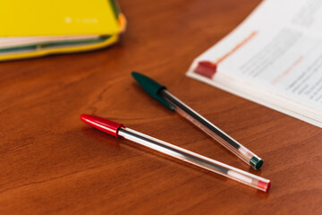 Two pens on a wooden table with a book and a yellow filing cabinet in the background