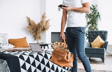 Man businessman with a phone in his hands and a travel bag at home or hotel near the bed, going on...