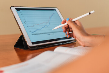Detail of student girl hand picking up a digital pen using a tablet at a table with a graph with books and pens