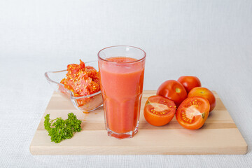 On a white background fresh tomatoes, a glass of juice and a bunch of parsley, in a sealed plate, waste seeds and peels, concept, freshly squeezed juice, a natural product at home