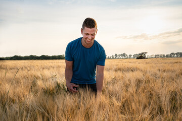 Ackerbau - junger, begeisterter Landwirt steht im Gegenlicht der Abendsonne im goldgelben Getreidefeld. 