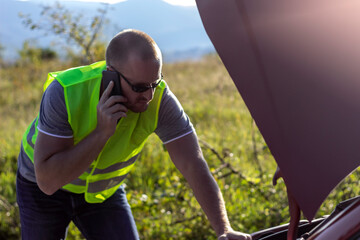 Shot of young man talking on phone near broken car on road.Caucasian man stand front broken car calling for assistance.Worried mature man calling on smartphone roadside assistance after breaking down.