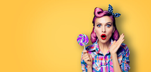 Purple head excited very surprised woman with lollipop. Pinup girl with wide opened mouth, eyes. Beauty model at retro fashion and vintage concept. Yellow orange color background with copy space.