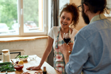Awesome food, awesome mood. Young woman looking at her boyfriend with a smile. Couple having toast, drinking wine and eating freshly baked pizza. Love, relationships concept