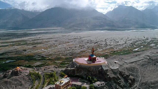 aerial dolly shot of a distant lord budha statue situated in the middle of a high altitude mountain valley.