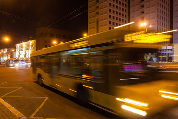 The motion of a blurred bus along the avenue in the evening