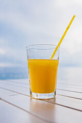 A glass of fresh orange juice with a straw against the blue sky is a refreshing summer drink on a hot day