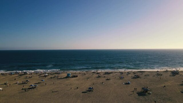 A Slow Aerial Dolly shot of Huntington Beach, California on a mildly busy day with people moving around and in the water.