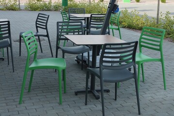 Fototapeta na wymiar green and black plastic chairs by the table stand on a gray sidewalk outside