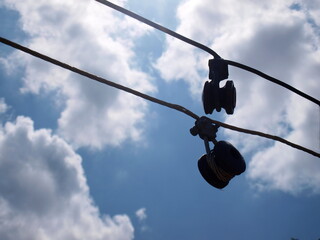Silhouette of insulators. Damaged electrical fuses hang on a potentially dangerous low voltage cable. On the blue sky background there are white clouds. Selective focus
