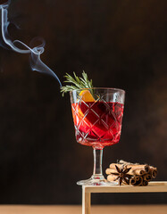Hot Christmas mulled wine cup on a creative stone podium on a dark background garnished with smoking rosemary sprigs.