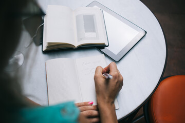 Cropped image of female writing affirmations checklist in textbook while planning visualisation productivity, selective focus on education equipment for exam preparation at table desktop