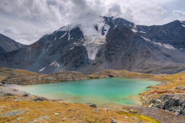 Obraz premium High mountain with a glacier. Green mountain lake. yellow grass. Autumn in the mountains.