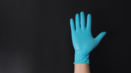 Hand wearing blue medical gloves doing five fingers number on black background.