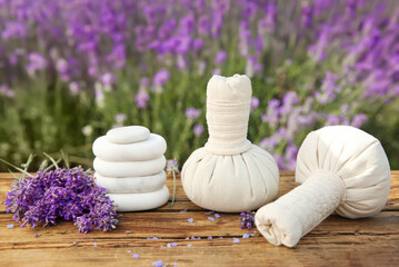 Fototapeta na wymiar Spa stones, fresh lavender flowers and herbal bags on wooden table outdoors, closeup